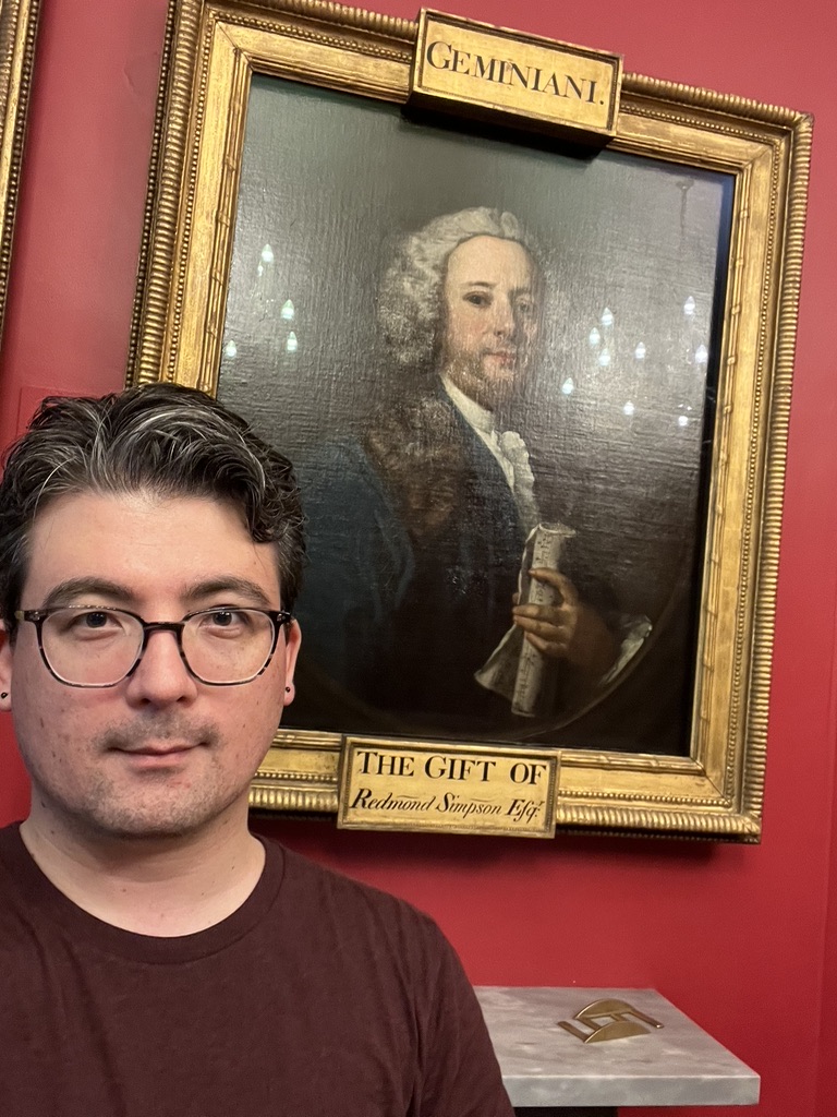 Jonathan Goya taking a selfie in front of an eighteenth-century portrait of Francesco Geminiani